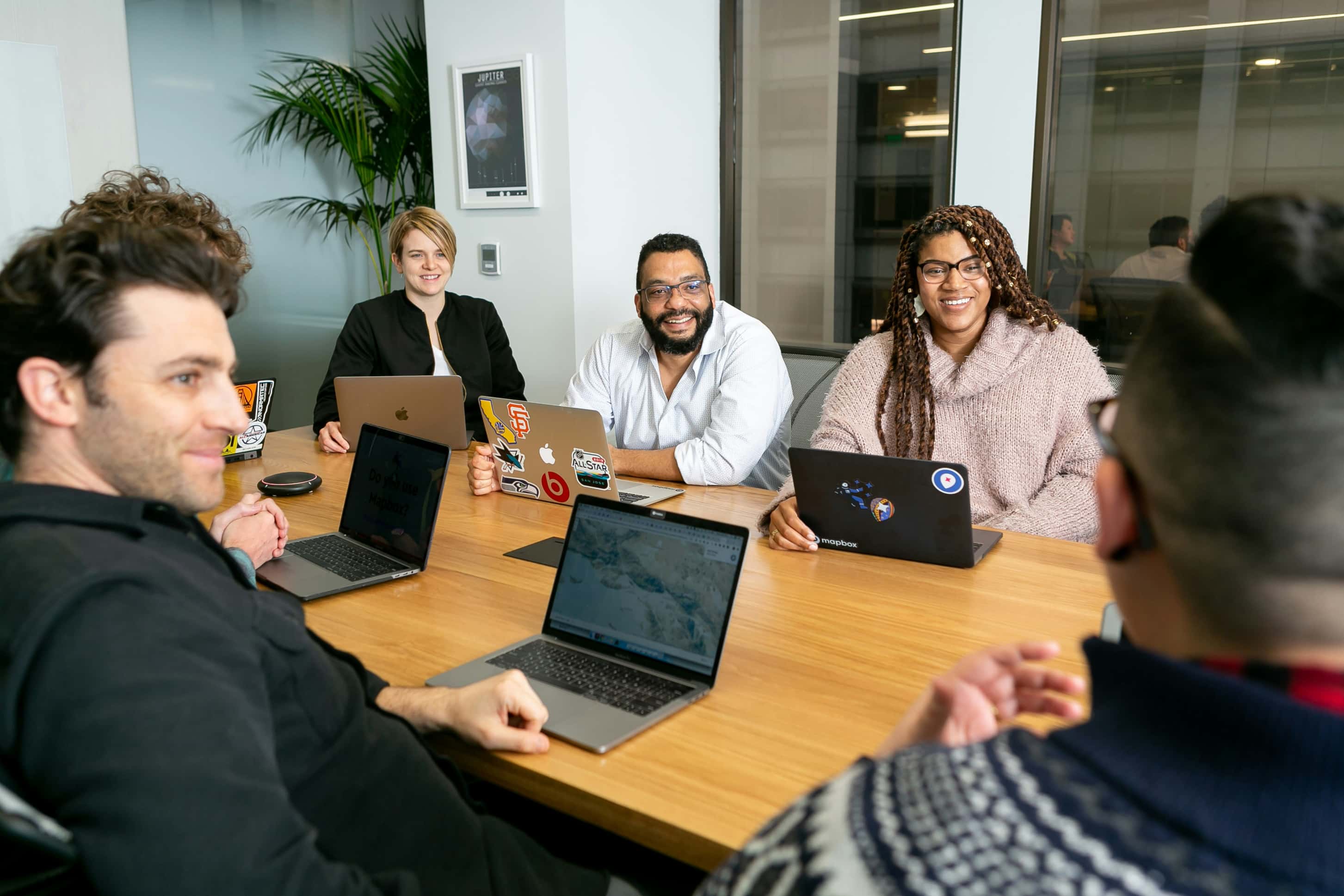 A few team members meet in a conference room, each with their laptops on the desks and smiling faces.